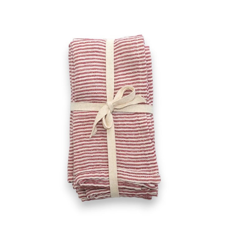 The RED STRIPE CLOTH NAPKIN by CREATIVE COOP is crafted from red and white striped cotton fabric, intricately folded into a bow shape. It is adorned with small red berries and green leaves, measures 18&quot; x 18&quot;, and includes a small white tag. This delightful napkin is available for individual purchase and displayed on a light gray surface.