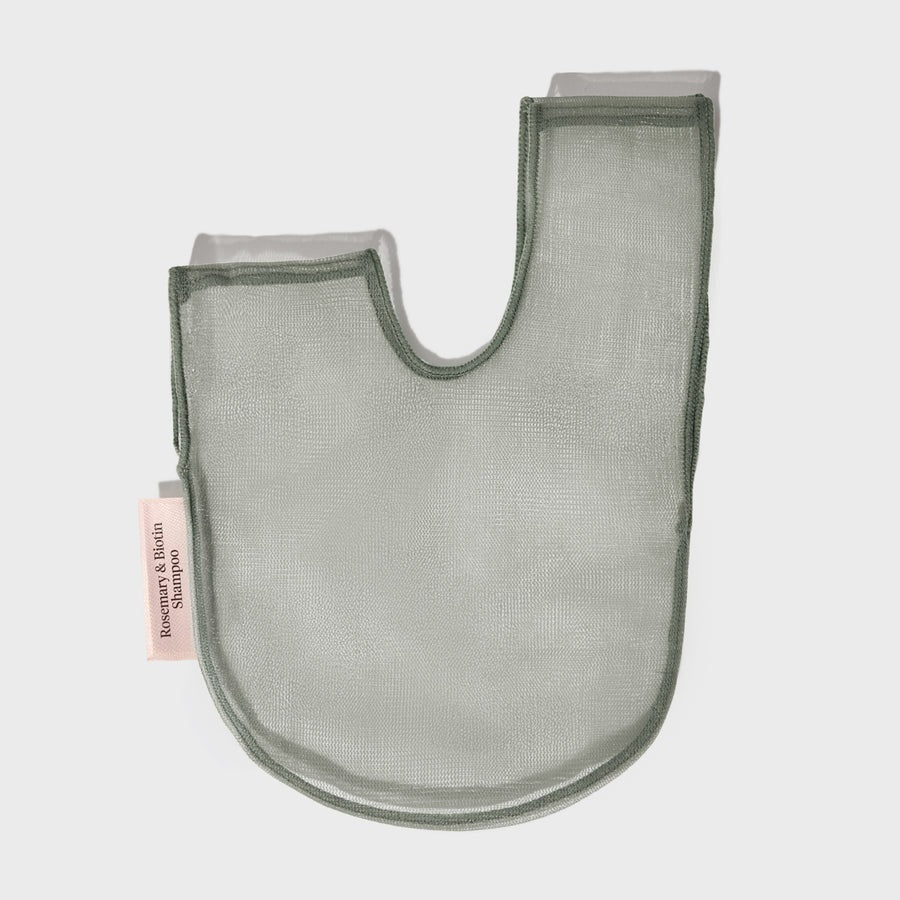 A green, eco-friendly mesh bag from KITSCH sits beside green packaging labeled “KITSCH - ROSEMARY & BIOTIN SHAMPOO BAR SAVER BAG,” designed for storing solid shampoo bars and extending their lifespan. A pink tag reads “Rosemary & Biotin Shampoo Bar.” Both the bag and box are displayed against a white background.