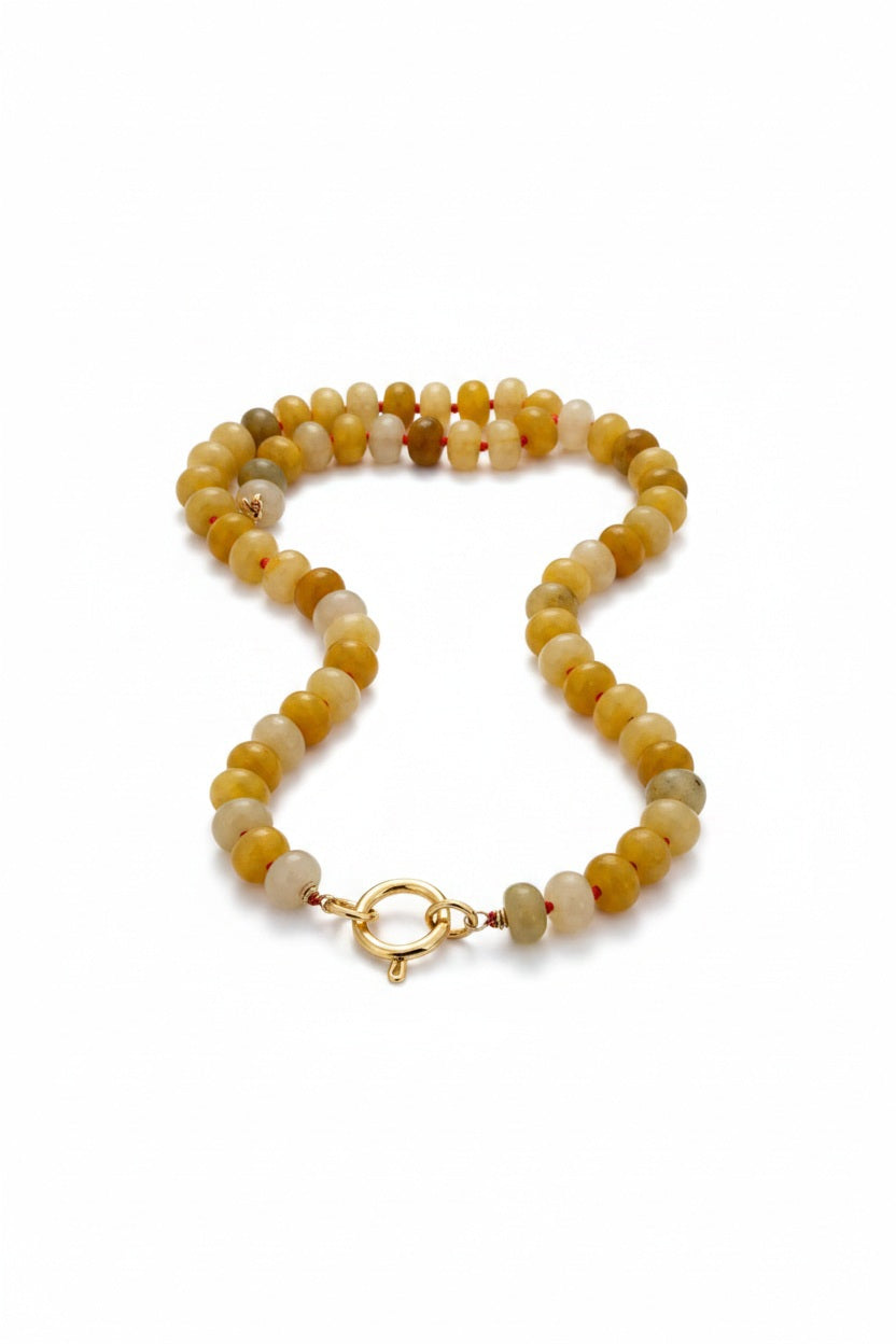THE ENERGY NECKLACE by SANDRINE FRANCE STUDIO features round, yellow Honey Jasper beads and a gold clasp. Handcrafted in NYC, this necklace is shown coiled in a loose oval shape on a white background.
