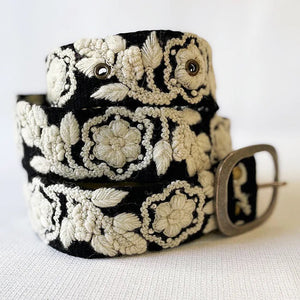 The JENNY KRAUSS Two Toned Belt in Black and Cream features intricate cream floral embroidery and a silver buckle, handmade in Peru. Shown coiled on a light background.