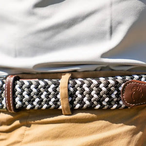 The ROOSTAS BAJA Woven Stretch Belt features a black, white, and gray tri-color weave, silver buckle, brown leather with white stitching, and an embossed ROOSTAS logo.