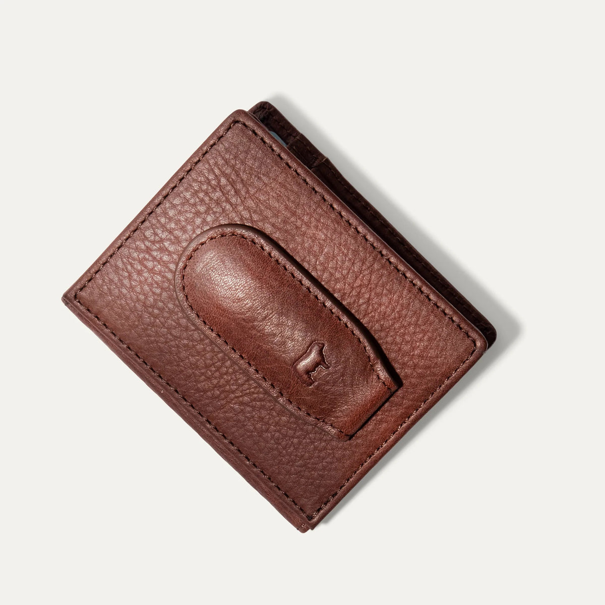 The WILL LEATHER GOODS Classic Money Clip sits atop an open full-grain leather wallet, both in brown, showcasing card slots against a plain light background.