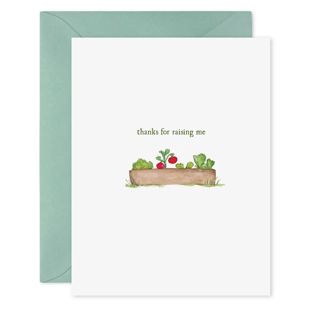 The E. FRANCES - THANKS FOR RAISING ME CARD by E. FRANCES PAPER is a hand-painted watercolor greeting card featuring a wooden garden bed with vegetables and the phrase &quot;thanks for raising me,&quot; paired with a light blue envelope.