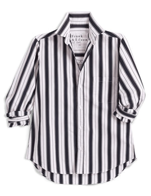 A woman stands outdoors in the sunlight, wearing the FRANK & EILEEN Waverly NYC Button Up Shirt in Italian Brushed Superluxe Cotton with black and tan stripes. The shirt features rolled-up sleeves, and she is buttoning or unbuttoning its perfectly tailored fit.