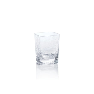 The ZODAX PUNTA MITA HAMMERED ROCKS GLASS is a 330 ml, clear, textured glass cup with a subtly square shape, displayed on a white background and reflecting light at its base.