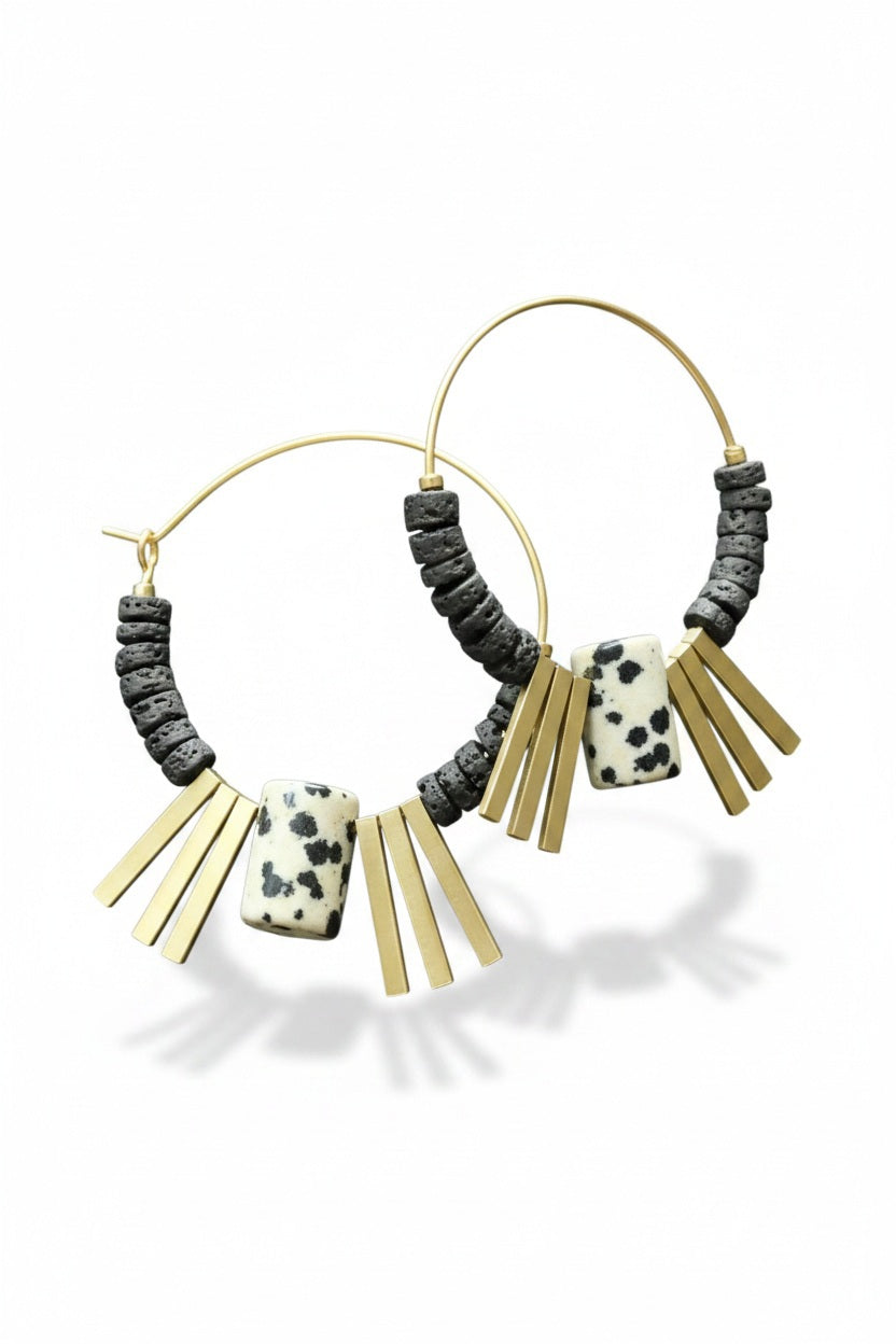 The DAVID AUBREY - Lava Bead and Dalmatian Jasper Hoop Earrings by DAVID AUBREY feature gold plated hoops adorned with black lava bead accents, a rectangular Dalmatian jasper stone, and multiple gold rectangular charms, beautifully displayed on a dark textured surface.