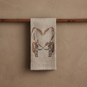SQUIRRELS WITH WHEAT HEART LINEN TEA TOWEL by CORAL & TUSK featuring two embroidered squirrels holding stalks of wheat that form a heart shape above them.