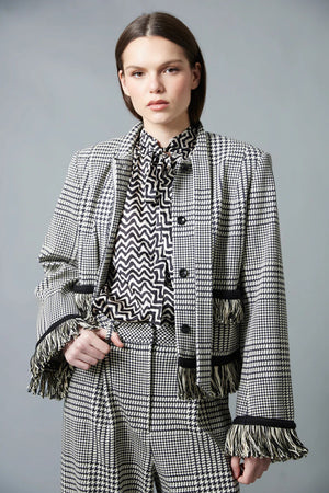A woman with straight brown hair faces away in a HOPE FOR FLOWERS Tie Neck Blouse—black and white, vertically striped Tencel with puffed sleeves—paired with wide-leg plaid trousers. The plain gray background reflects sustainable style.