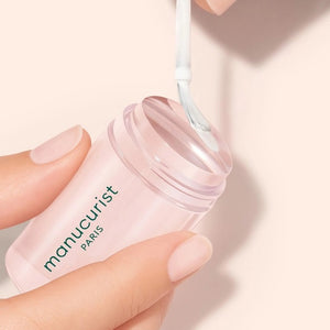 A hand with a light pink French manicure rests beside the MANUCURIST - MANI STAMPER by MANUCURIST INC on a pale background.