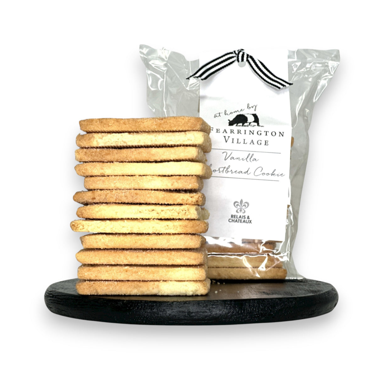 A stack of buttery and crisp vanilla shortbread cookies is displayed on a black serving board in front of a clear package labeled &quot;Fearrington House Signature Collection - Housemade Vanilla Shortbread Cookies&quot; with a black and white striped ribbon tie at the top. These delectable treats could easily be found at The Fearrington House Restaurant.