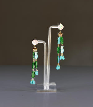 The SANDRINE FRANCE STUDIO - EVIE EARRINGS feature handmade round mother-of-pearl studs, gold connectors, green and blue fish charms, and turquoise teardrop beads at the ends.