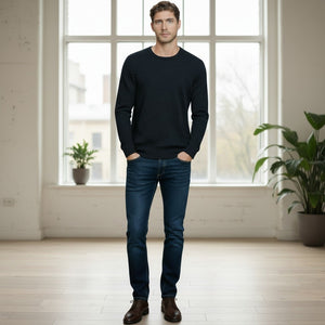 A man with short brown hair stands with his hands in his pockets against a white background, wearing the AUTUMN CASHMERE - Cashmere Basic Crew Neck with Rib Bottom in Midnight and blue jeans.