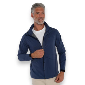 A man wearing the CRIQUET - Watershed Rain Jacket in Navy stands outdoors on a rainy day, with trees and wet pavement in the background.