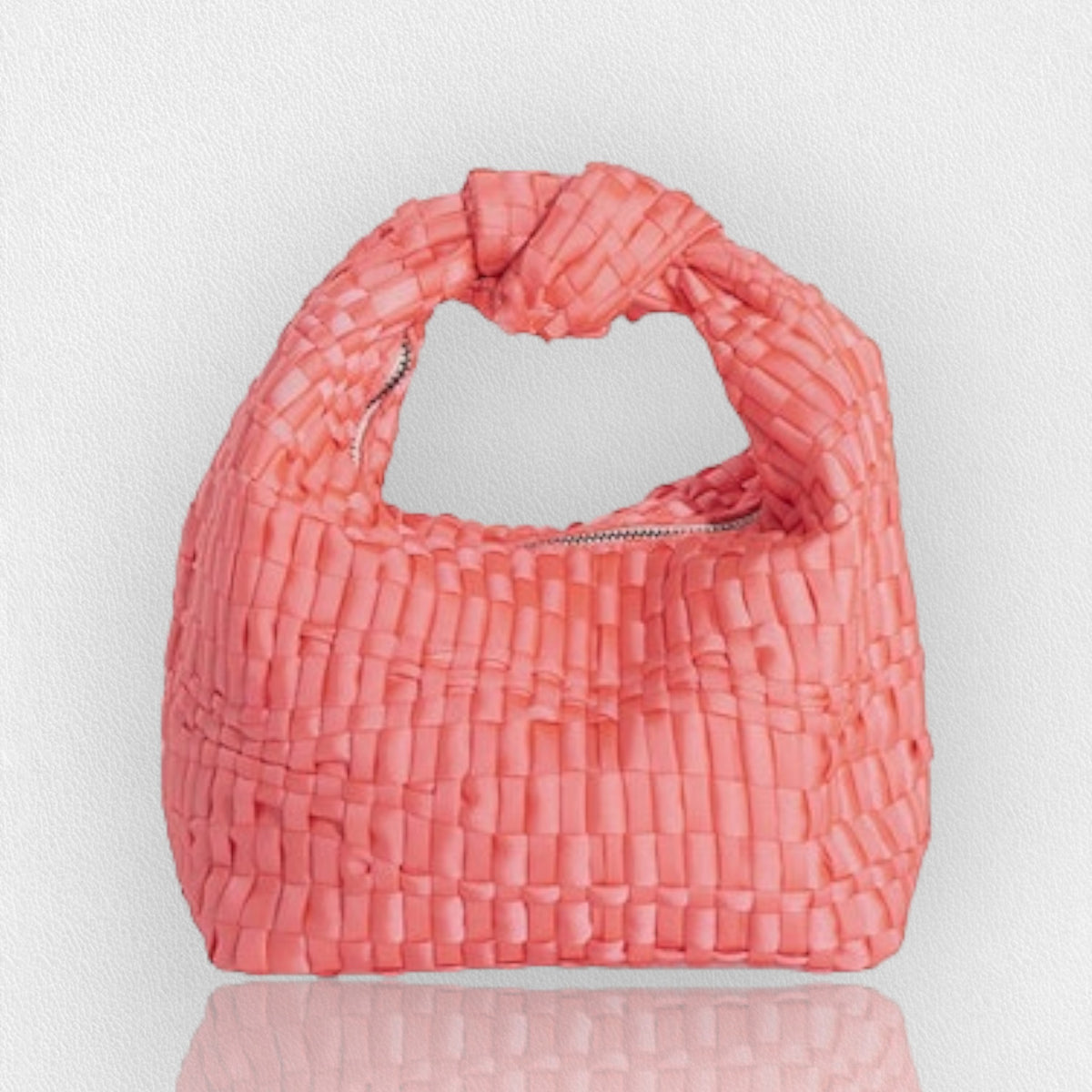 The MINI KNOT HANDLE BAG by MARIA LA ROSA is a compact and chic accessory crafted from light blue ribbon fabric. It features a distinctive knotted handle at the top and is photographed on a reflective surface, enhancing its slight sheen. Handmade in Italy, this unique bag stands out against a plain, light gray background.