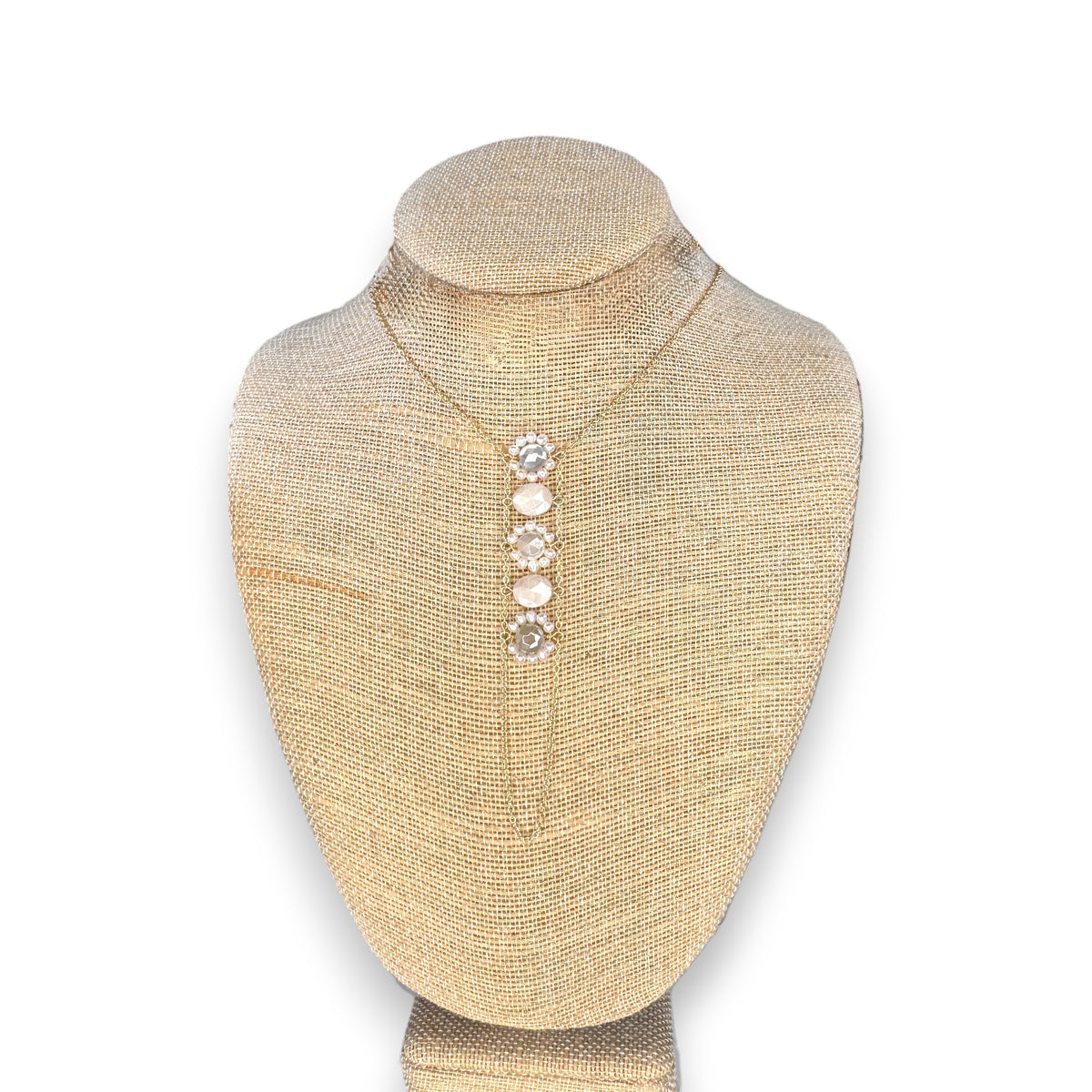 A beige necklace display stand showcases the GOLDISH - FLOWER WHITE MOONSTONE AND WHITE PEARL LADDERS TO BLISS NECKLACE, featuring five gemstones in a vertical, sacred geometry-inspired design. The plain white background enhances its elegance.