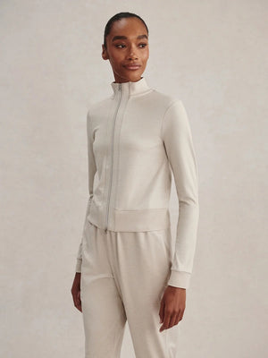 A person wears a light beige Varley Rufus Cropped Zip Through Sweat in Pebble Marl with a high collar and matching pants.
