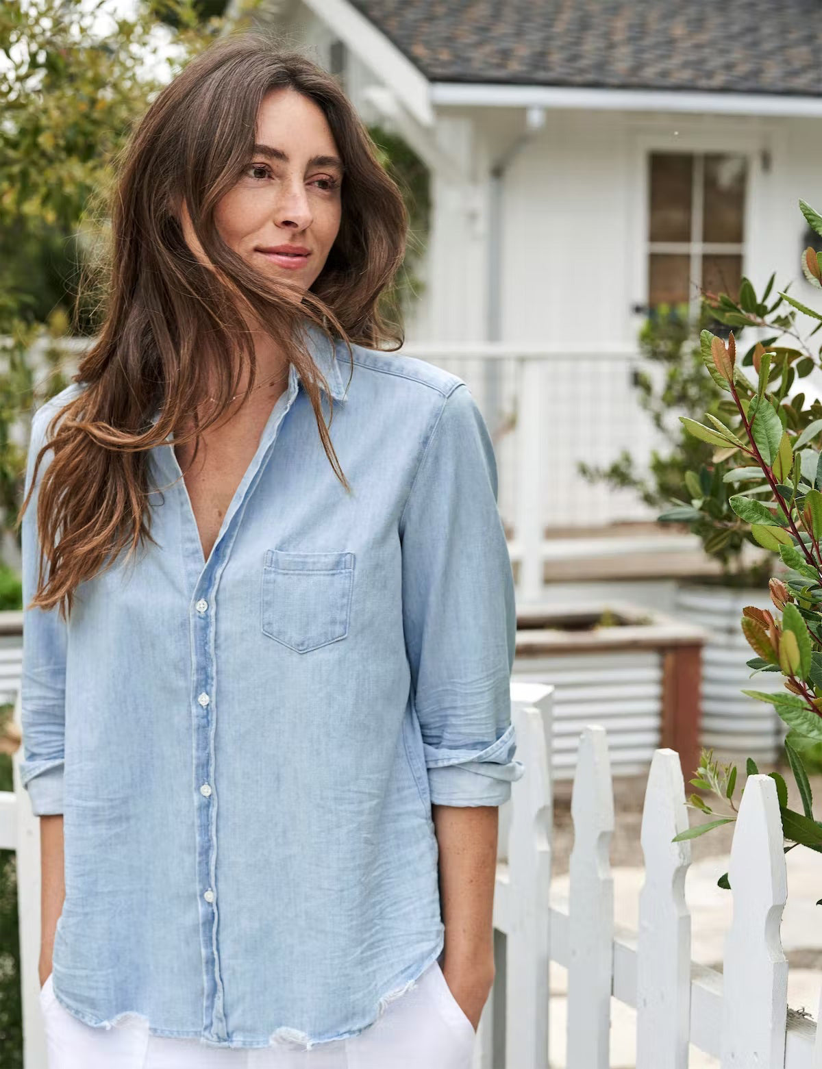 A light blue denim button-up shirt is displayed against a plain white background. The FRANK AND EILEEN - EILEEN RELAXED BUTTON UP CLASSIC WASH FAMOUS DENIM shirt features a relaxed fit, long sleeves rolled up to mid-forearm, a single chest pocket, and a slightly curved hem. Known for its bust-flattering button placement, the label inside reads &quot;Frank &amp; Eileen EST 1947.