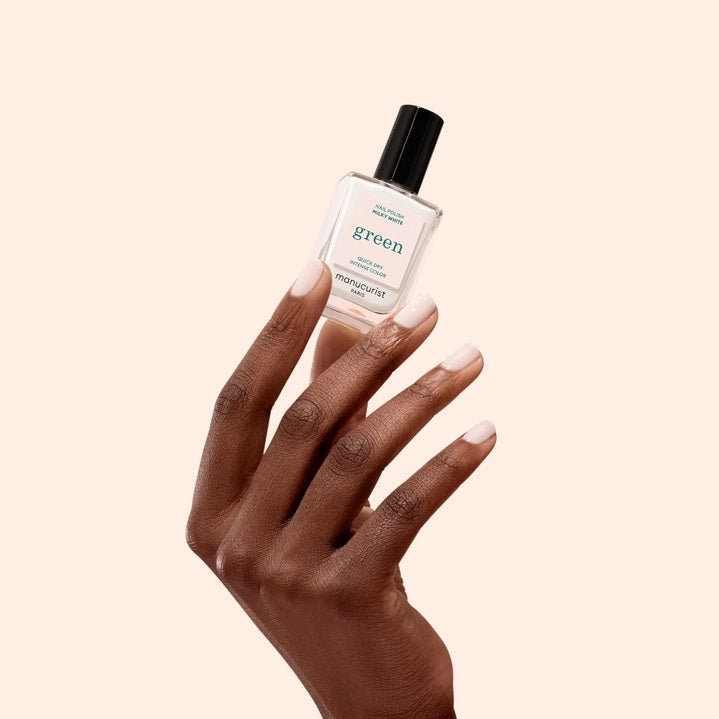 A hand adorned with MANUCURIST - GREEN™ NAIL POLISH IN MILKY WHITE by MANUCURIST INC rests on a soft yellow leather purse, set against a backdrop of cream-colored textured fabric.