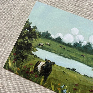 Bring the countryside to your home with the SOPHIE WYATT STUDIO - WILD MEADOWS & BELTIES ART PRINT (12x16). This fine art print by SOPHIE WYATT STUDIO depicts a serene scene where a Belted Galloway cow stands amid wildflowers beside a tranquil pond, while more cows graze in the distant field. Lush bushes frame the landscape and white fluffy clouds float across a vivid blue sky, perfectly capturing the peaceful charm of rural life.