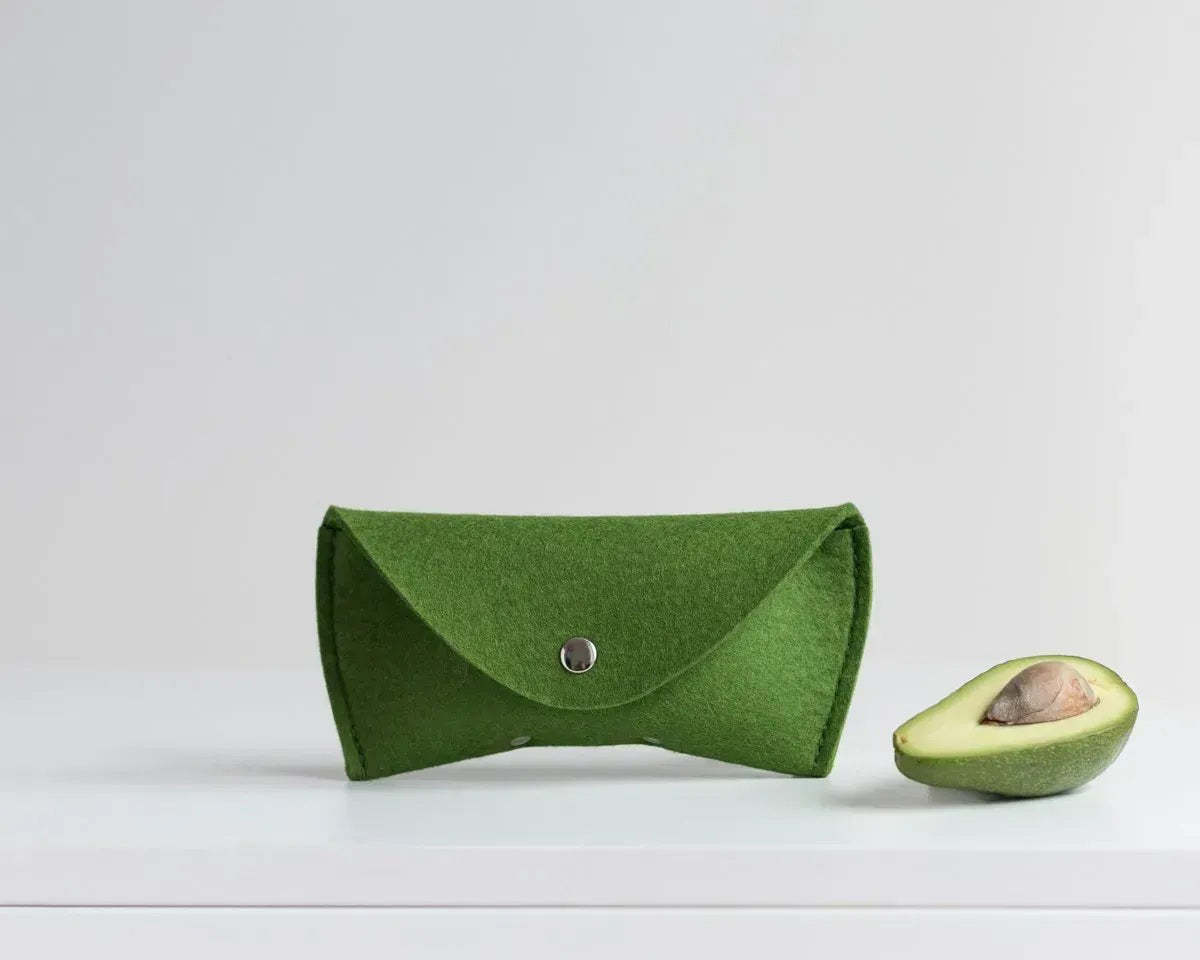 Three WOOLBERRY WOOL FELT GLASSES CASES in navy, bright, and light blue with magnetic closures are arranged on a white surface near clear sunglasses, framed by white-blue hydrangeas.