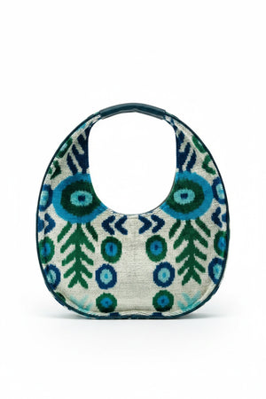 The BALDIZ LUCA BAG IN AQUA VINE is a circular handbag with a short handle, showcasing bold blue and green abstract shapes and leaves on a light background—perfect for everyday use and inspired by the signature style of BALDIZ.