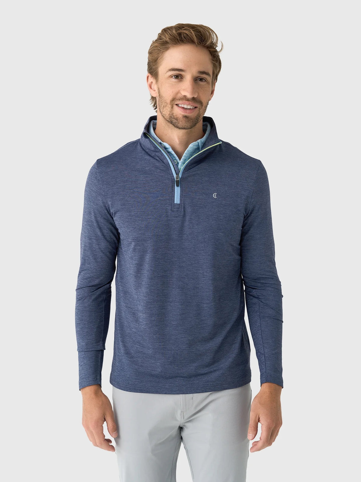 A person wears a CRIQUET - FEATHER PERFORMANCE KNIT QUARTER ZIP PULLOVER over a light blue checkered shirt. The moisture-wicking brrr° pullover by CRIQUET features a small embroidered logo on the left chest. Only the upper torso and neck are visible.