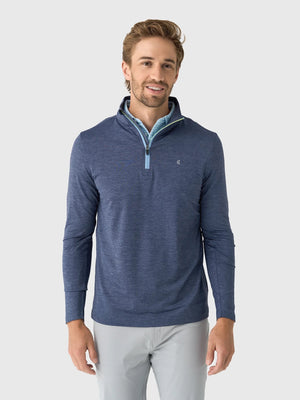 A person wears a CRIQUET - FEATHER PERFORMANCE KNIT QUARTER ZIP PULLOVER over a light blue checkered shirt. The moisture-wicking brrr° pullover by CRIQUET features a small embroidered logo on the left chest. Only the upper torso and neck are visible.