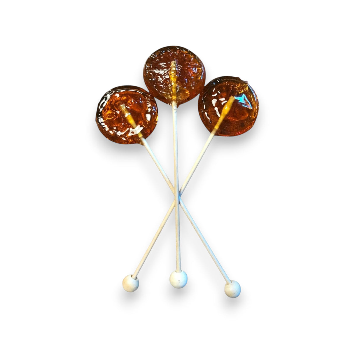 Three CLOISTER HONEY - HONEY LOLLIPOPS, caramel-colored and round with white sticks, are arranged in a crisscross pattern against a plain white background. These lollipops from CLOISTER HONEY have a glossy, translucent appearance, perfect for an afternoon snack.