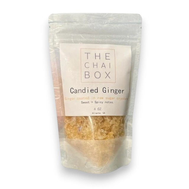 A close-up image of a square white plate containing small, beige-colored, crystal-like granules that appear to be THE CHAI BOX - CANDIED GINGER. The granules have a slightly translucent appearance.