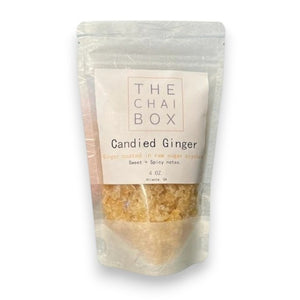 A close-up image of a square white plate containing small, beige-colored, crystal-like granules that appear to be THE CHAI BOX - CANDIED GINGER. The granules have a slightly translucent appearance.