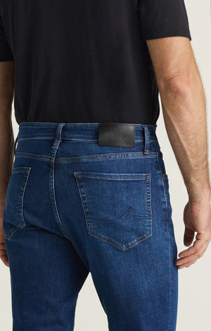 A person is shown from the back wearing a black shirt and the 34 HERITAGE - CASH BOOTCUT JEANS IN DARK BRUSHED VINTAGE by 34 HERITAGE. The vintage denim features back pockets and a black leather patch on the waistband, with the wearer’s arms visible.