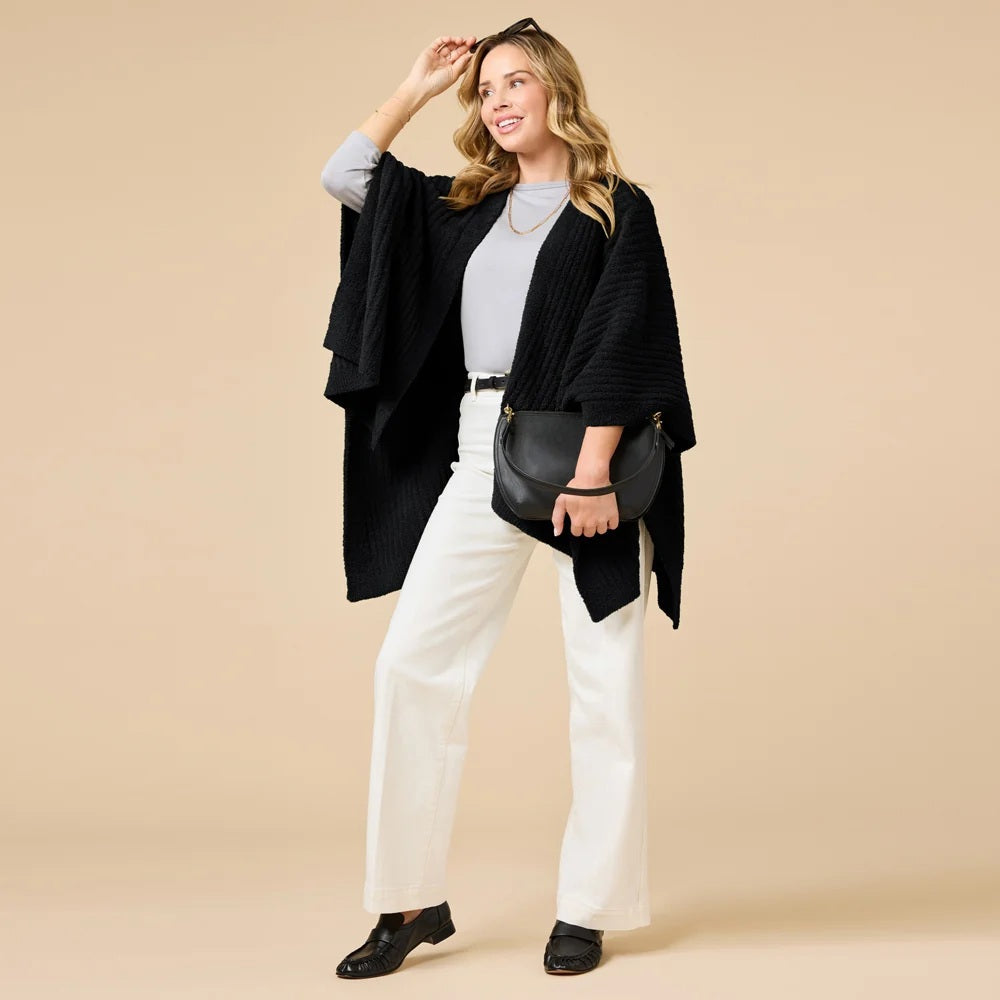 A woman wearing a black SOFTIES - SOLID RIB MARSHMALLOW SHAWL over a grey top and white trousers.