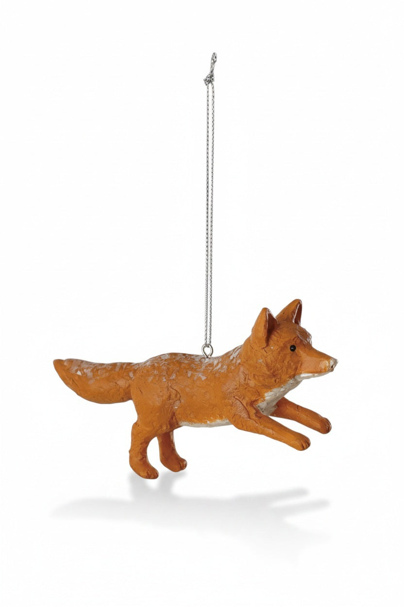 A small resin VINTAGE FOX ORNAMENT stands on a stack of textured paper in front of a woodland decor illustration featuring three green pine trees.