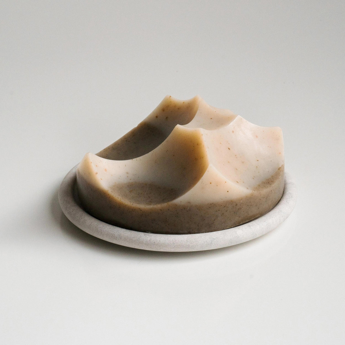 The UME - GREY BOUTON ERODE SOAP DISH by UME STUDIO features a large, round, white button design with three holes resting on a light gray tray, serving as a subtle decorative accent.