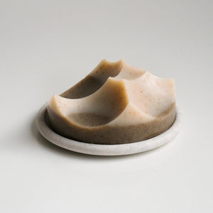 The UME - GREY BOUTON ERODE SOAP DISH by UME STUDIO features a large, round, white button design with three holes resting on a light gray tray, serving as a subtle decorative accent.