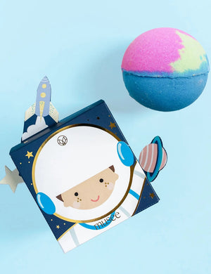 The MUSEE - YOU’RE OUT OF THIS WORLD BATH BALM from MUSEE rests next to its vibrant space-themed box, which features a smiling cartoon astronaut and a rocket on top, highlighting the playful appeal of natural bath products.