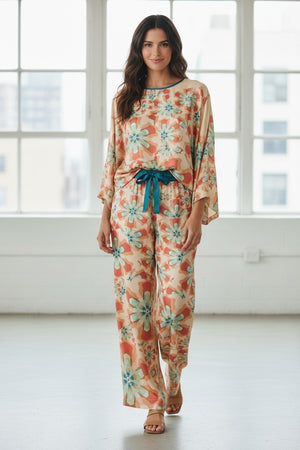 The FRANCO FERRARI - WIDE SLEEVE CORAL BLOUSE features a flowy, lightweight silk design with a floral print in teal, orange, and beige. Perfect for vacation dressing, it has a slightly sheer fabric with a round neckline and back button closure.