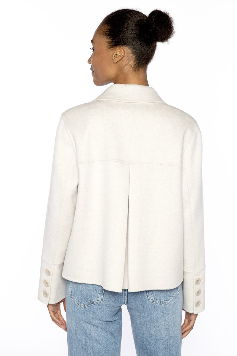 A woman in the KINROSS CASHMERE Pleat Back Short Cashmere Blend Coat in navy stands against a white background, smiling softly with one hand touching the collar and wearing blue jeans.