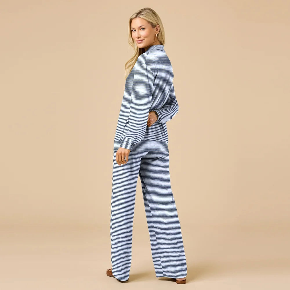A woman wears a navy blue SOFTIES - DREAM JERSEY COWL NECK LOUNGE SET consisting of a long-sleeved top and wide-leg trousers.