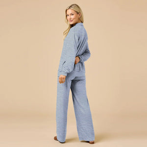 A woman wears a navy blue SOFTIES - DREAM JERSEY COWL NECK LOUNGE SET consisting of a long-sleeved top and wide-leg trousers.