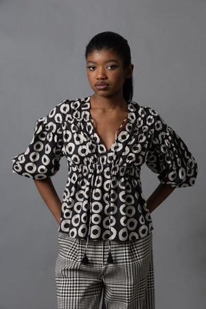 A person with long brown hair, seen from behind, wears the HOPE FOR FLOWERS Shirred Blouse and loose, dark green cargo pants with large pockets, standing against a plain gray background.