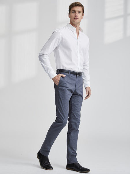 A man stands in a minimalist room wearing the FRANK &amp; EILEEN FINBAR Men's Button Up Shirt in Classic Italian Poplin, tucked into slim-fit blue trousers with a black belt and dress shoes, looking to the side with a neutral expression.
