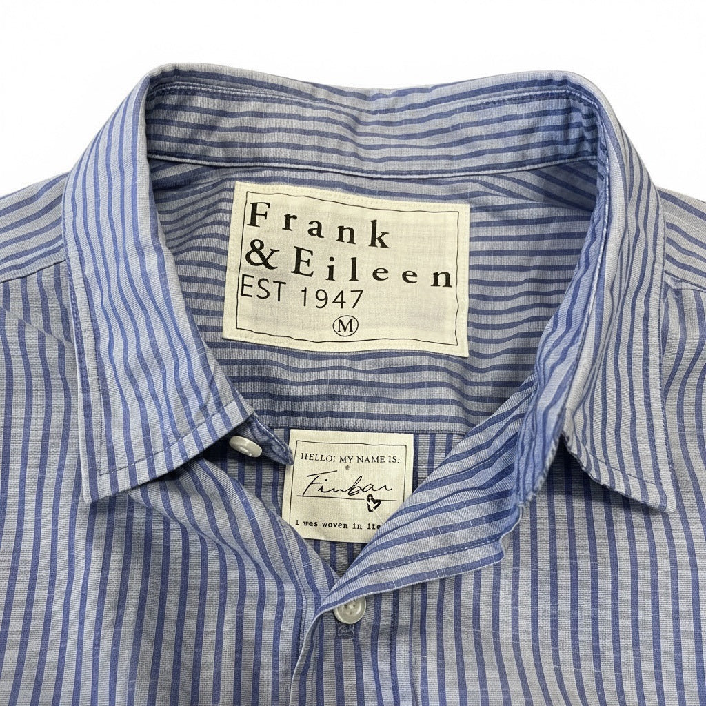 A man in a FRANK &amp; EILEEN Finbar Men's Button Up Shirt in Blue Stripes, blue jeans, and white sneakers walks confidently down a sunny, tree-lined cobblestone street.