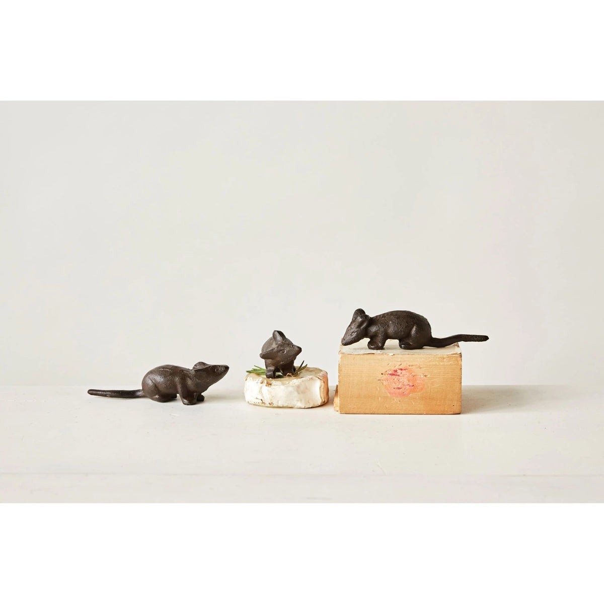 Positioned against a plain white background are three small, dark brown &quot;CAST IRON MOUSE&quot; figurines by CREATIVE COOP. Each measuring 5 inches in length, these figurines feature varied poses and detailed features, conveying a rustic and playful aesthetic through their assorted styles.