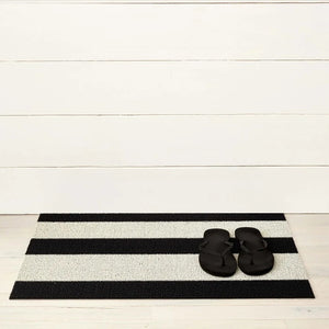 The CHILEWICH Black and White Bold Stripe Shag Doormat, measuring 18x28, features a rectangular design with alternating horizontal black and white stripes, offering an easy-care solution perfect for both indoor and outdoor use.