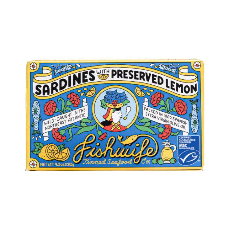 A vibrant, rectangular tin of FISHWIFE - SARDINES &amp; PRESERVED LEMON from the Fishwife brand. The label showcases lively illustrations of sardines, a lemon, and decorative elements. It highlights that the sustainably wild-caught sardines are sourced from the Northeast Atlantic and packed in Spanish extra virgin olive oil. Net weight: 4.2 oz.