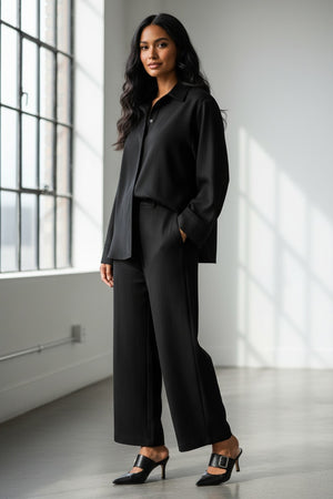 Facing away from the camera, a person wears MILVA’s MILVA MI - TUXEDO DRESS PANT in dark green with cropped legs and black heels, holding a black handbag. The background is solid brown.