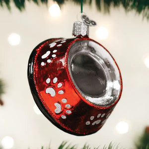 An OLD WORLD CHRISTMAS DOG BOWL ORNAMENT that is red, bowl-shaped, and decorated with white paw prints.
