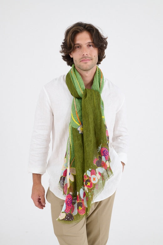 A person with medium-length brown hair, wearing a white button-up shirt and the STORIATIPIC - AZURE SCARF by STORIATIPIC, featuring colorful patterns and handmade embroidery, smiles softly against a plain white background.