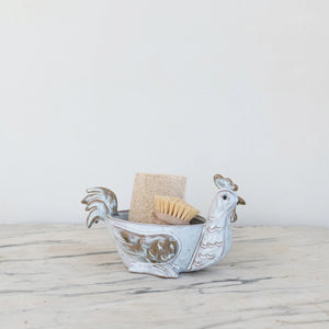 The CREATIVE COOP STONEWARE CHICKEN SHAPED BOWL is a ceramic bowl designed like a chicken with detailed tail, wings, and comb. It has a glossy finish in white and brown due to its reactive glaze, making it perfect as a quirky kitchen sponge holder.